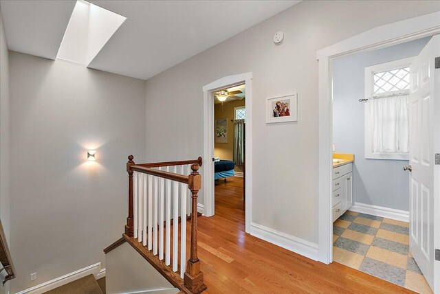 corridor with light wood-style floors, baseboards, and an upstairs landing