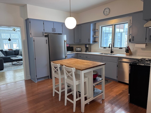 kitchen featuring a kitchen island, appliances with stainless steel finishes, wood finished floors, pendant lighting, and a sink