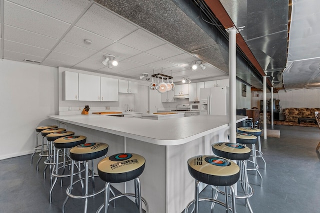 kitchen with a paneled ceiling, white appliances, white cabinets, a kitchen bar, and kitchen peninsula