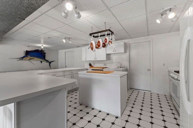 kitchen featuring kitchen peninsula, white appliances, sink, white cabinets, and a center island