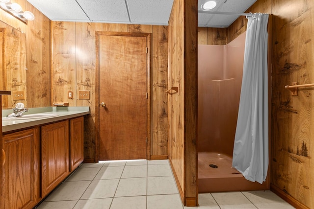 bathroom with a drop ceiling, walk in shower, tile patterned floors, wooden walls, and vanity