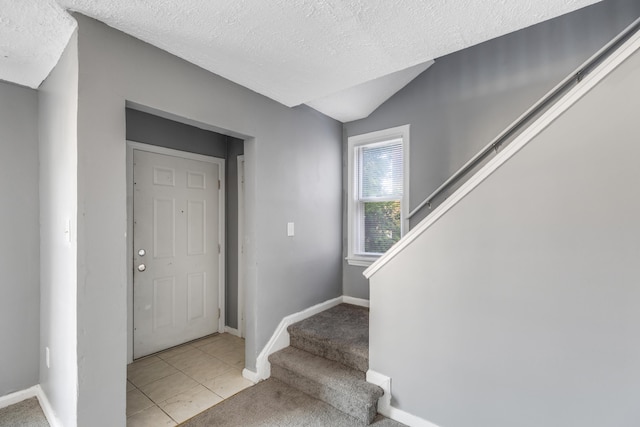 foyer entrance with light tile patterned floors, a textured ceiling, and lofted ceiling