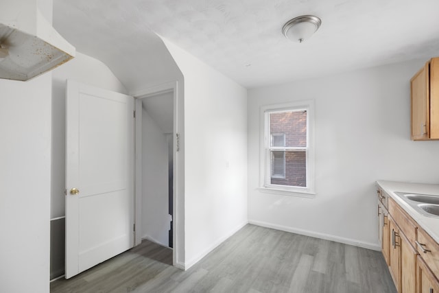 kitchen featuring light brown cabinetry, vaulted ceiling, and light hardwood / wood-style flooring