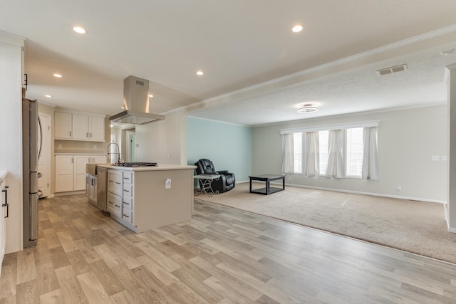 kitchen with a center island with sink, appliances with stainless steel finishes, range hood, light colored carpet, and white cabinetry