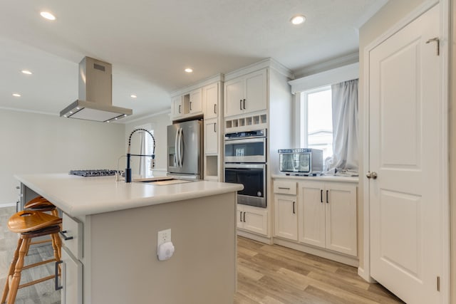 kitchen with an island with sink, range hood, light hardwood / wood-style floors, white cabinetry, and stainless steel appliances