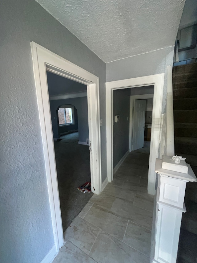 corridor with a textured ceiling, a textured wall, and baseboards