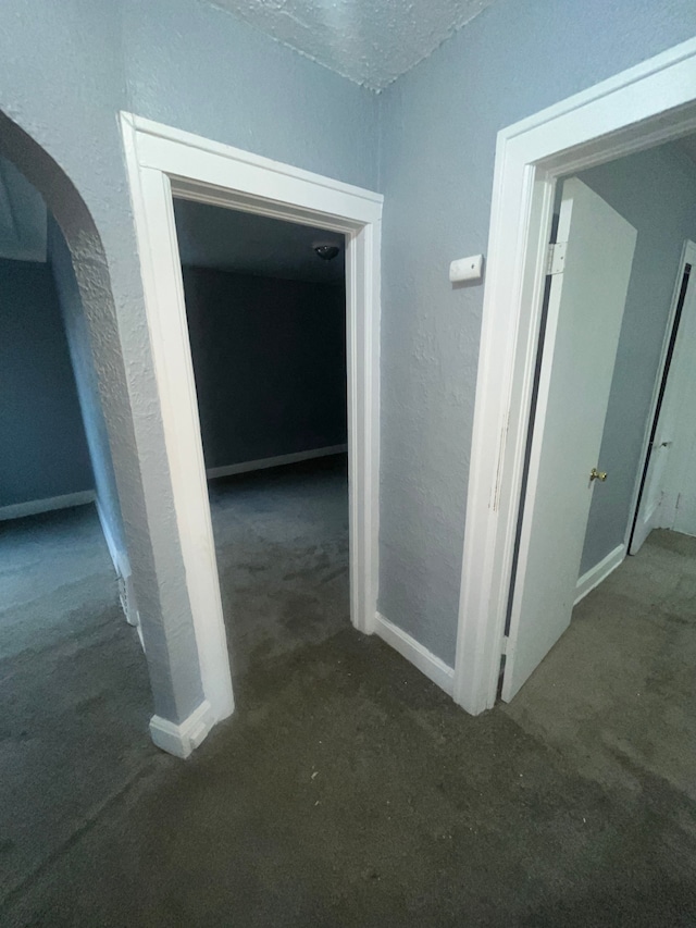 hall with a textured ceiling and dark carpet