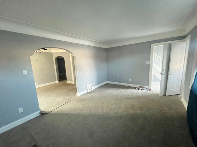 carpeted spare room with baseboards, visible vents, and arched walkways