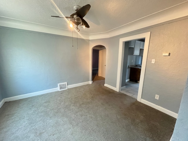carpeted empty room featuring a textured wall, a textured ceiling, arched walkways, visible vents, and a ceiling fan