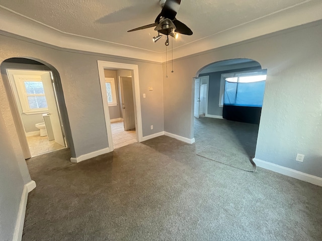 carpeted empty room featuring arched walkways, a textured ceiling, ceiling fan, and baseboards