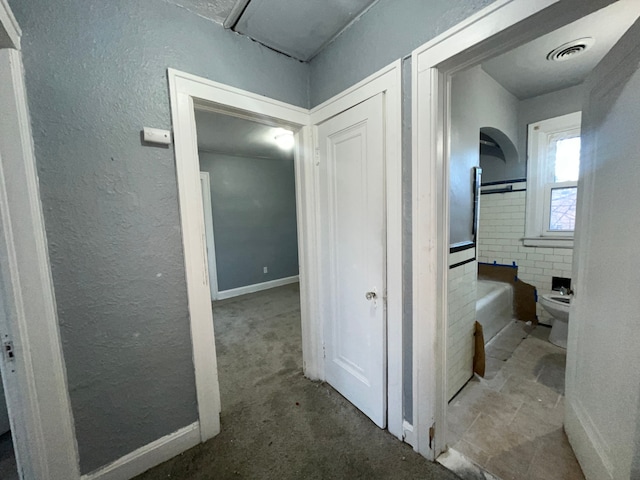 hallway featuring a textured wall, carpet, arched walkways, and visible vents