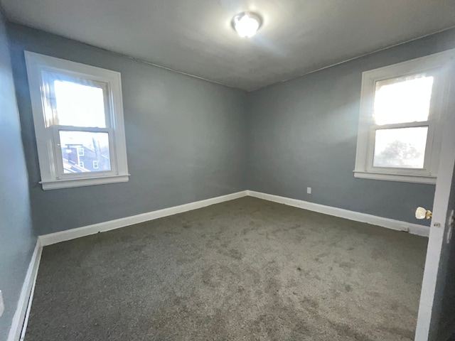 empty room featuring baseboards and dark colored carpet