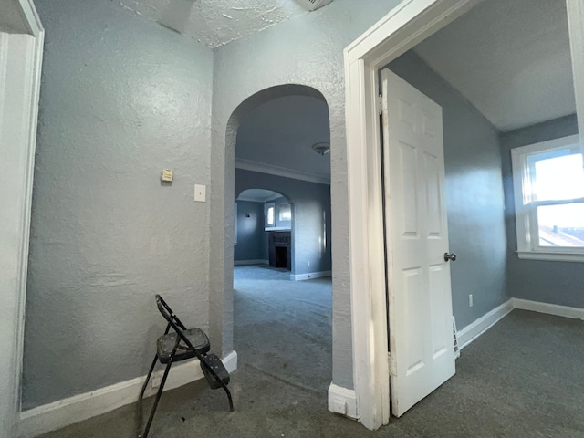 hallway with arched walkways, baseboards, carpet flooring, and a textured wall