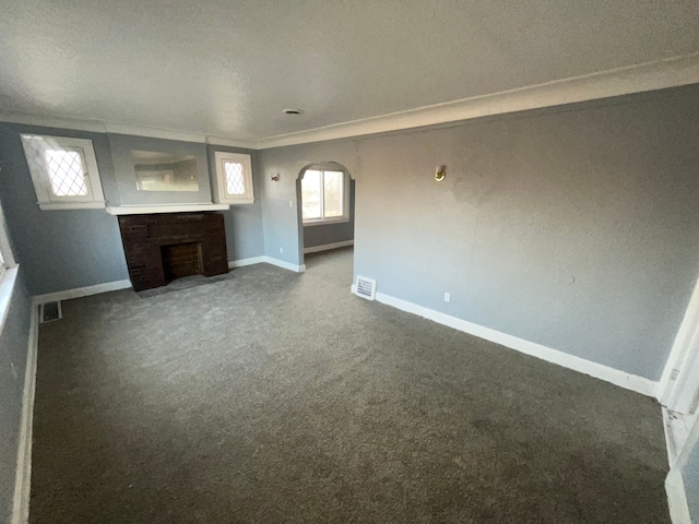 unfurnished living room with carpet flooring, baseboards, arched walkways, visible vents, and a brick fireplace