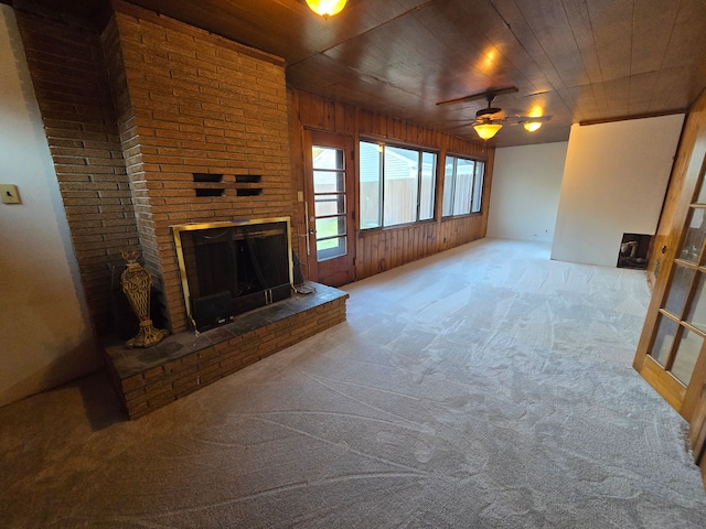 unfurnished living room with ceiling fan, wooden ceiling, a brick fireplace, wooden walls, and carpet