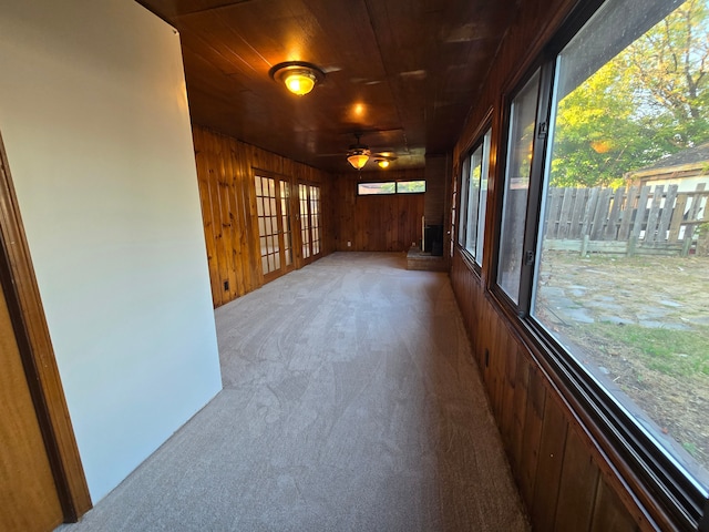 carpeted empty room with ceiling fan, wooden ceiling, and wood walls