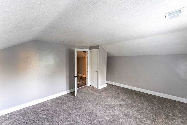 additional living space with dark colored carpet, lofted ceiling, and a textured ceiling