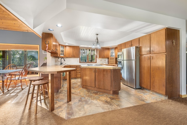 kitchen featuring a center island, appliances with stainless steel finishes, a tray ceiling, decorative light fixtures, and light colored carpet