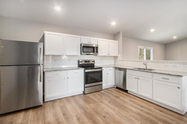 kitchen featuring white cabinets, sink, light stone countertops, light wood-type flooring, and stainless steel appliances