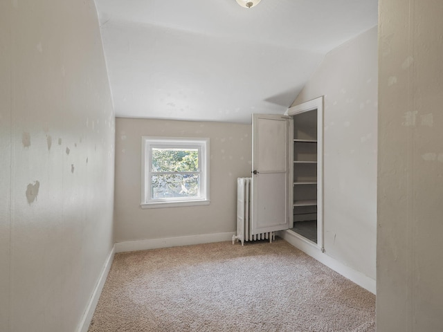 spare room featuring radiator, light carpet, and lofted ceiling