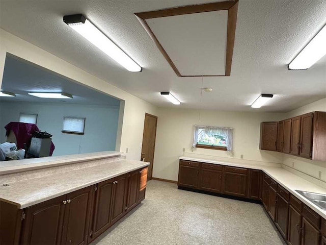 kitchen with dark brown cabinets, sink, kitchen peninsula, and a textured ceiling