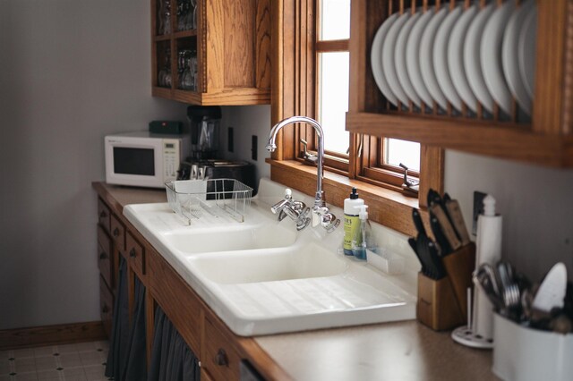 5721 Broomhead Rd, Williamsburg, MI 49690 - kitchen with white microwave, brown cabinetry, glass insert cabinets, a sink, and tile countertops