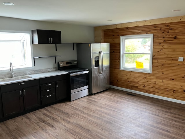 kitchen with appliances with stainless steel finishes, light wood-type flooring, wood walls, and sink