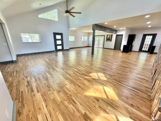 unfurnished living room with high vaulted ceiling, light hardwood / wood-style flooring, ceiling fan, and a healthy amount of sunlight