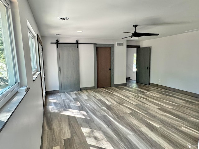 unfurnished bedroom featuring ceiling fan, a barn door, and wood-type flooring