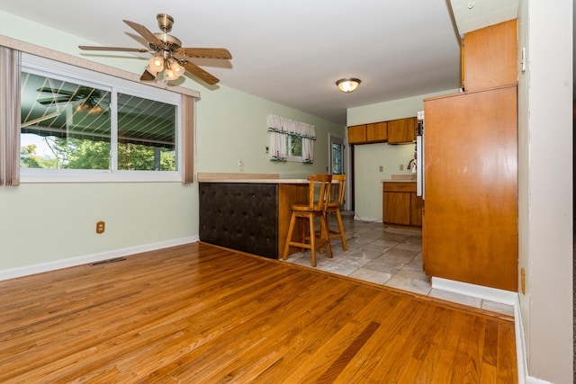 kitchen featuring a breakfast bar area, kitchen peninsula, ceiling fan, and light hardwood / wood-style flooring