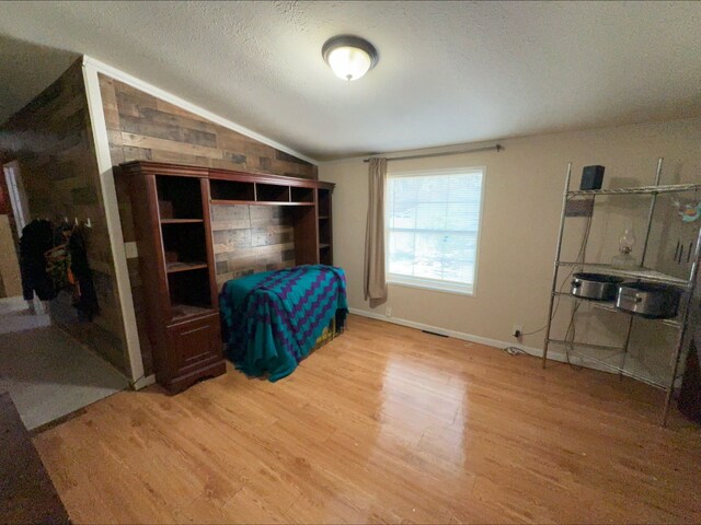 bedroom with a textured ceiling, hardwood / wood-style floors, and lofted ceiling