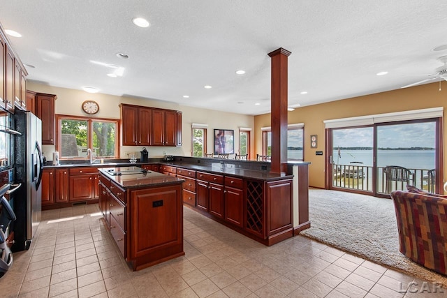 kitchen with kitchen peninsula, ornate columns, a textured ceiling, a water view, and a kitchen island