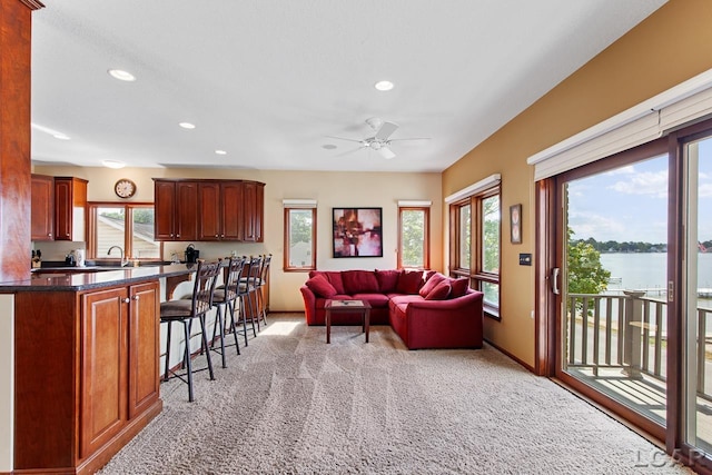 carpeted living room with sink, a water view, plenty of natural light, and ceiling fan