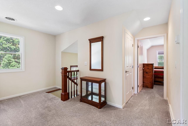 corridor with light carpet, lofted ceiling, and a healthy amount of sunlight