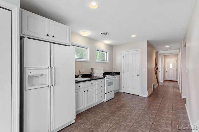 kitchen featuring sink, white cabinets, dark tile patterned flooring, and white appliances