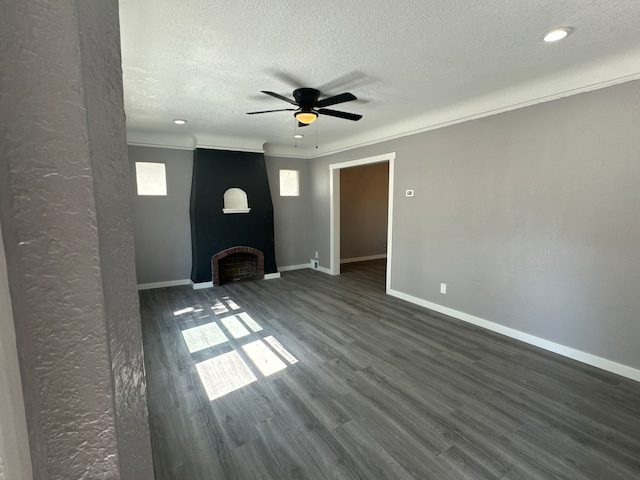 unfurnished living room with dark hardwood / wood-style flooring, a textured ceiling, ceiling fan, crown molding, and a fireplace