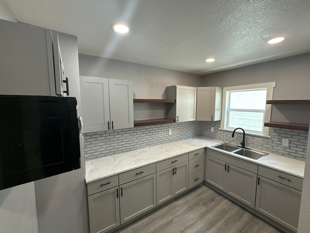 kitchen featuring gray cabinetry, sink, decorative backsplash, light hardwood / wood-style floors, and light stone counters