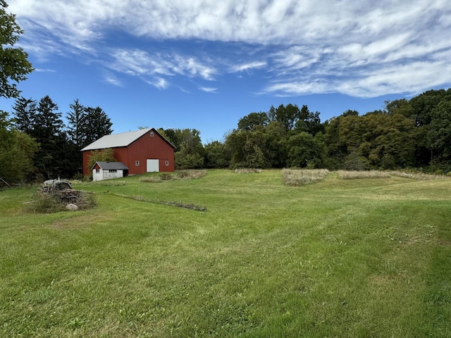 5295 Belding Rd NE, Rockford, MI 49341 - view of grassy yard featuring a detached garage, an outbuilding, driveway, and a forest view
