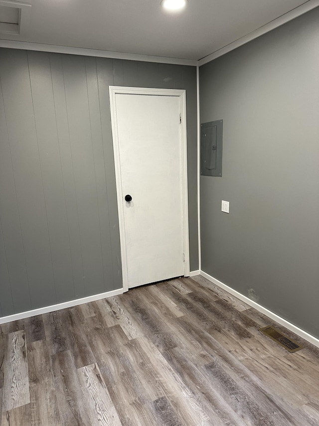 empty room featuring wood-type flooring, crown molding, and electric panel