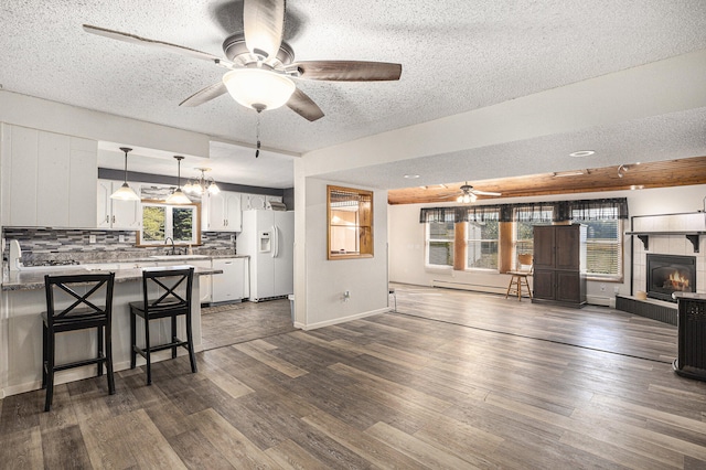 kitchen featuring a textured ceiling, dark wood-type flooring, decorative light fixtures, white cabinetry, and white fridge with ice dispenser