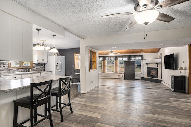 kitchen featuring a kitchen breakfast bar, a textured ceiling, white cabinetry, and white fridge with ice dispenser