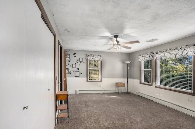 unfurnished bedroom featuring ceiling fan, carpet floors, multiple windows, and a baseboard heating unit