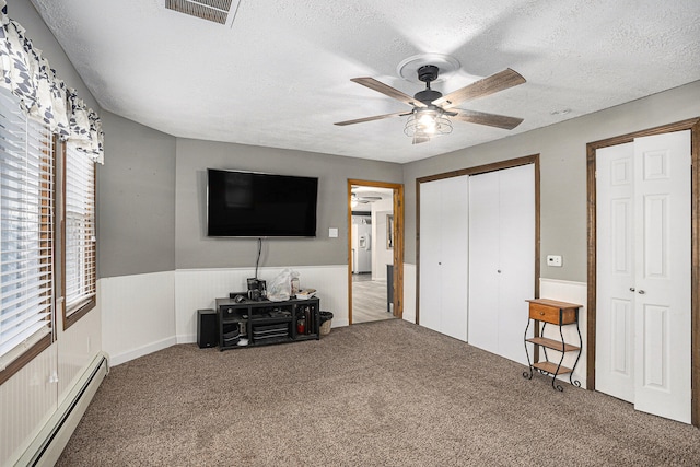 carpeted bedroom featuring a textured ceiling, baseboard heating, multiple closets, and ceiling fan