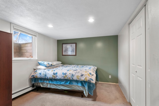 carpeted bedroom with a closet, a textured ceiling, and a baseboard heating unit