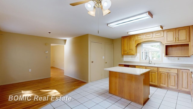 kitchen featuring ceiling fan, sink, backsplash, a kitchen island, and light wood-type flooring