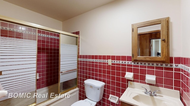 full bathroom featuring toilet, vanity, tile walls, and combined bath / shower with glass door