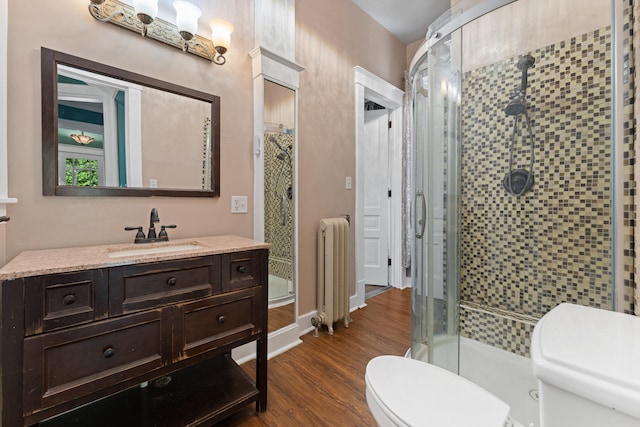 bathroom featuring radiator, toilet, vanity, a shower with shower door, and hardwood / wood-style flooring