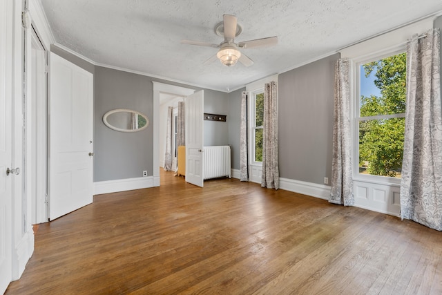 unfurnished bedroom featuring hardwood / wood-style floors, ceiling fan, radiator, and multiple windows