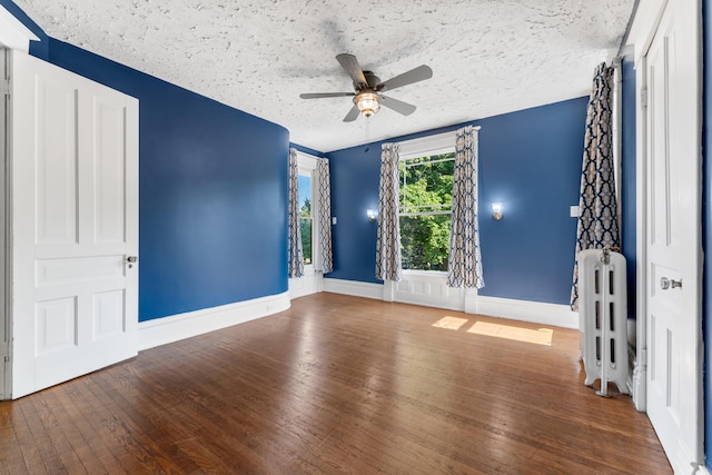 unfurnished room with ceiling fan, radiator heating unit, wood-type flooring, and a textured ceiling