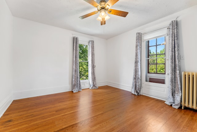 unfurnished room with ceiling fan, wood-type flooring, and radiator heating unit